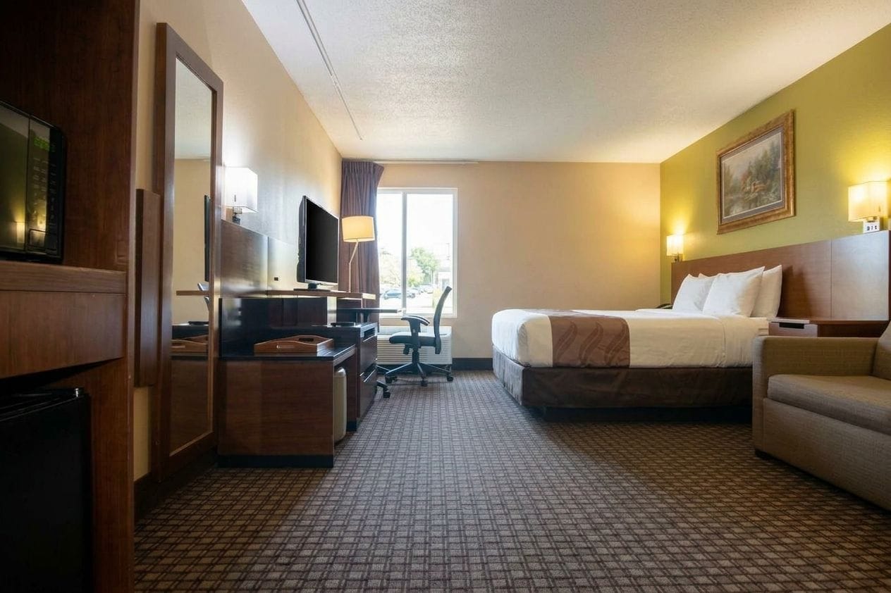 A hotel room with a bed, a desk with a computer, a television, and a sofa.