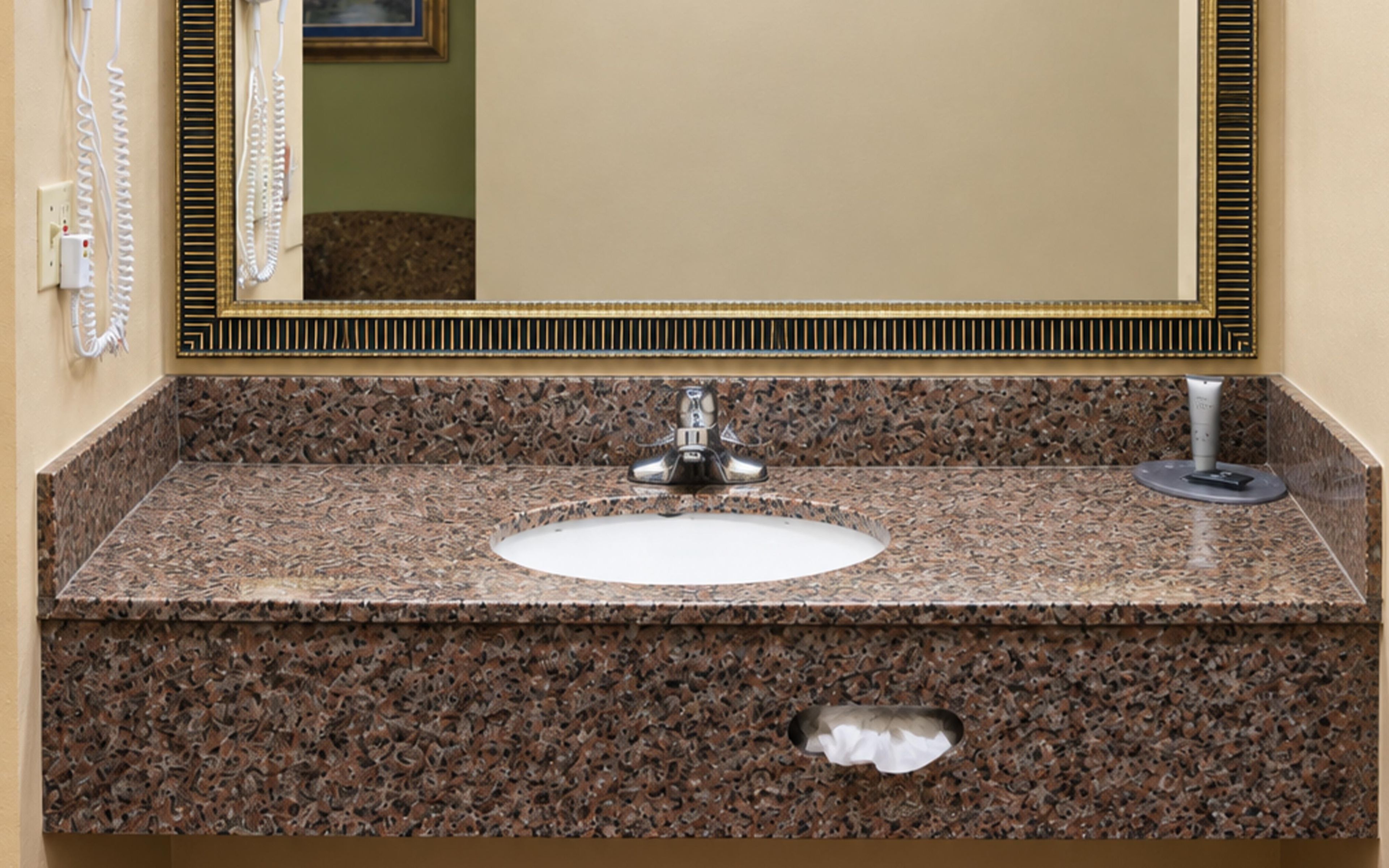 A bathroom with a granite countertop, a sink, a mirror, and a towel dispenser.