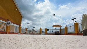 Zona de playa con un edificio amarillo, barandillas blancas y sombrillas.