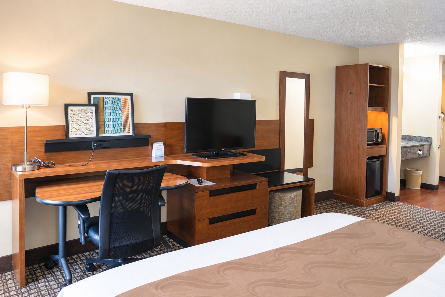 A hotel room with a bed, desk, chair, television, and a mirror.