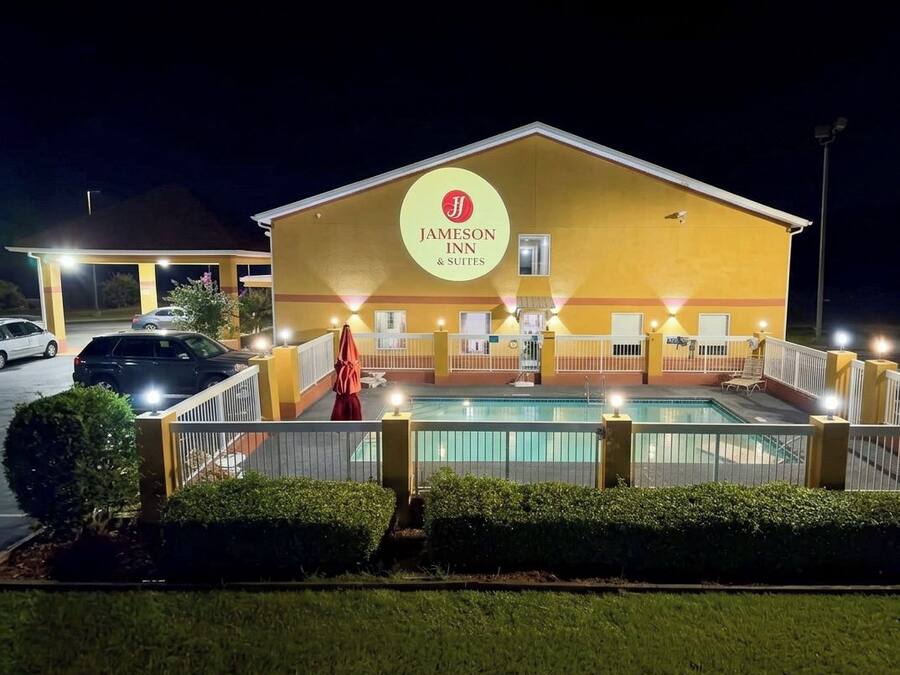 Un Jameson Inn & Suites con piscina, mobiliario exterior e una fachada bien iluminada.