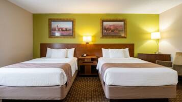 A hotel room with two beds, a wooden headboard, a nightstand, a lamp, and two framed pictures on the wall.