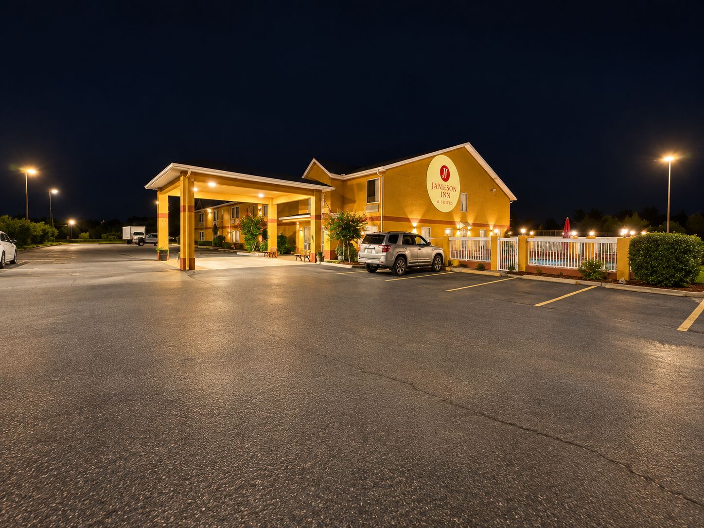 Vestíbulo de hotel bien iluminado con estacionamiento, camino de entrada con portón y un vehículo visible.