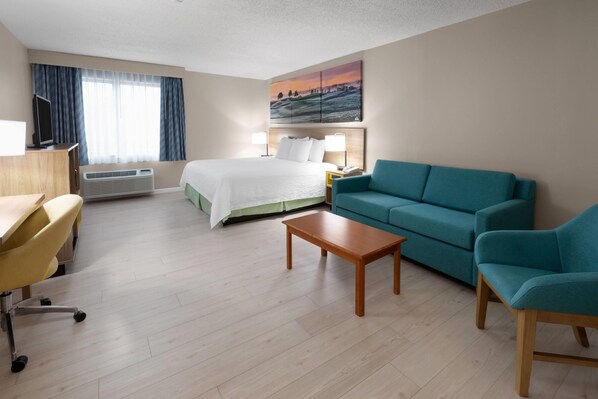 A hotel room with a bed, a desk, a chair, a sofa, and a painting on the wall. - Days Inn & Suites by Wyndham Seaford (Seaford)