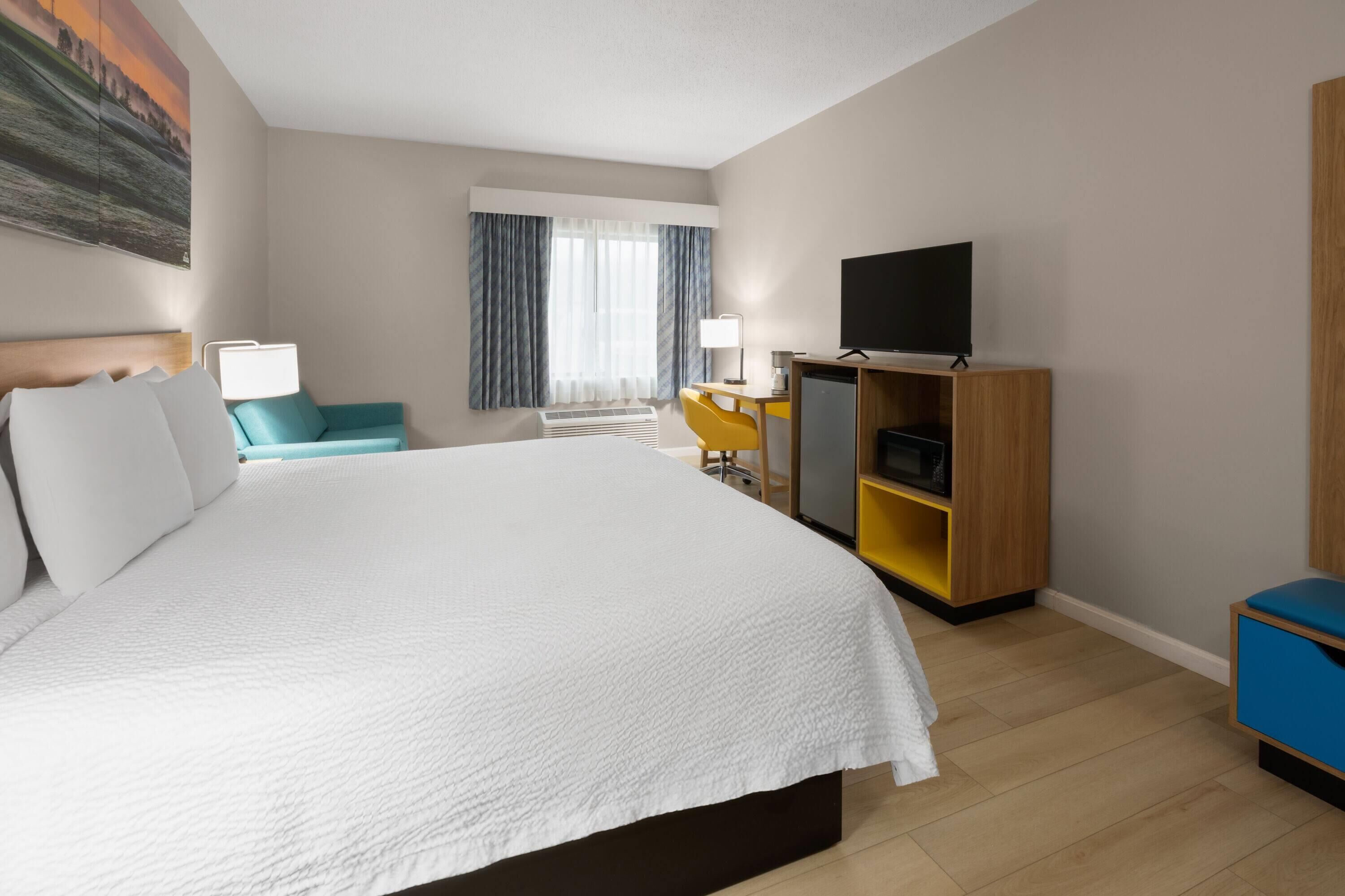 A hotel room with a large bed, a desk with a TV, a chair, and a wardrobe.