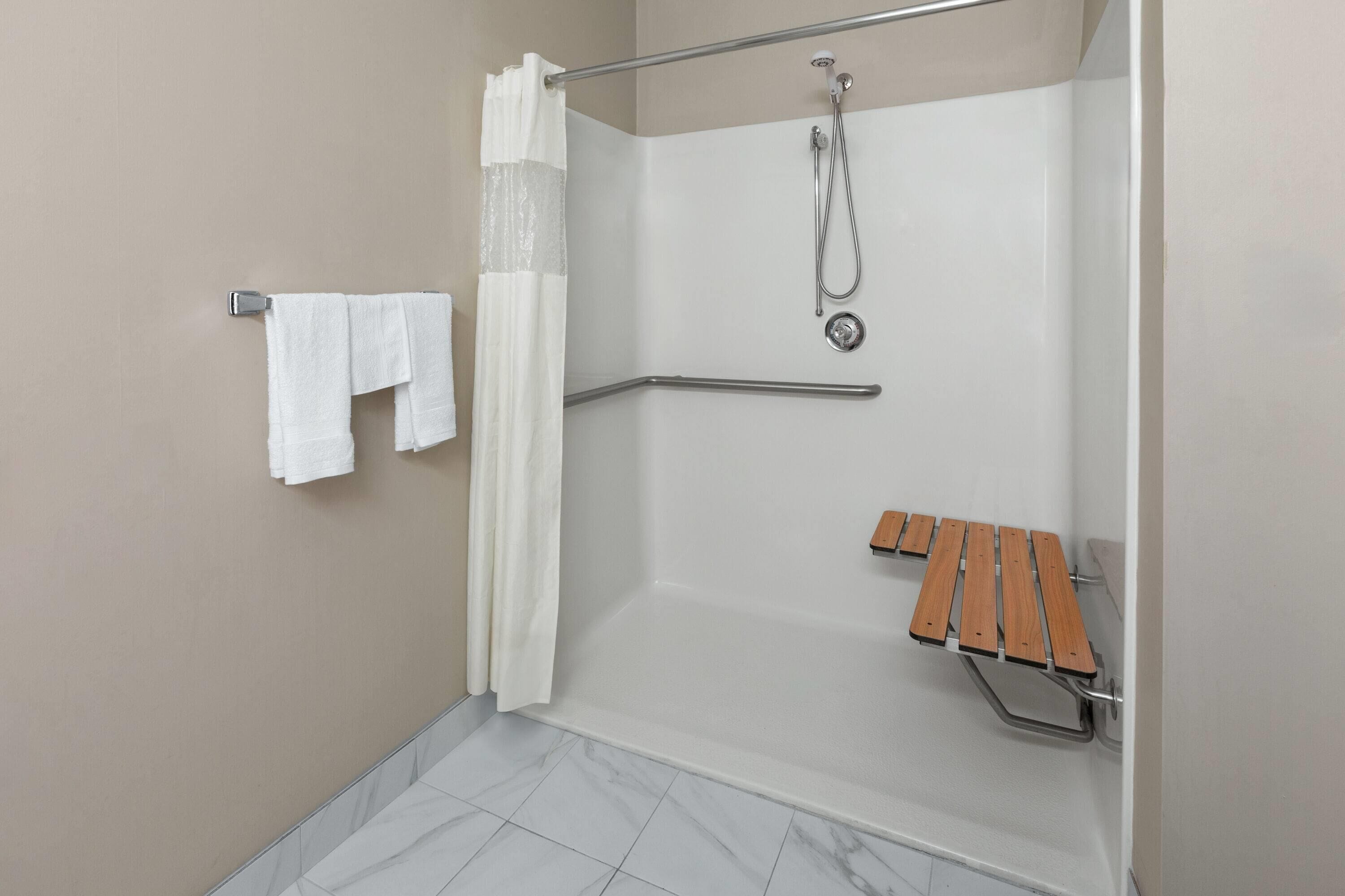 A shower area with a grab bar, a wooden bench, and a towel rack.