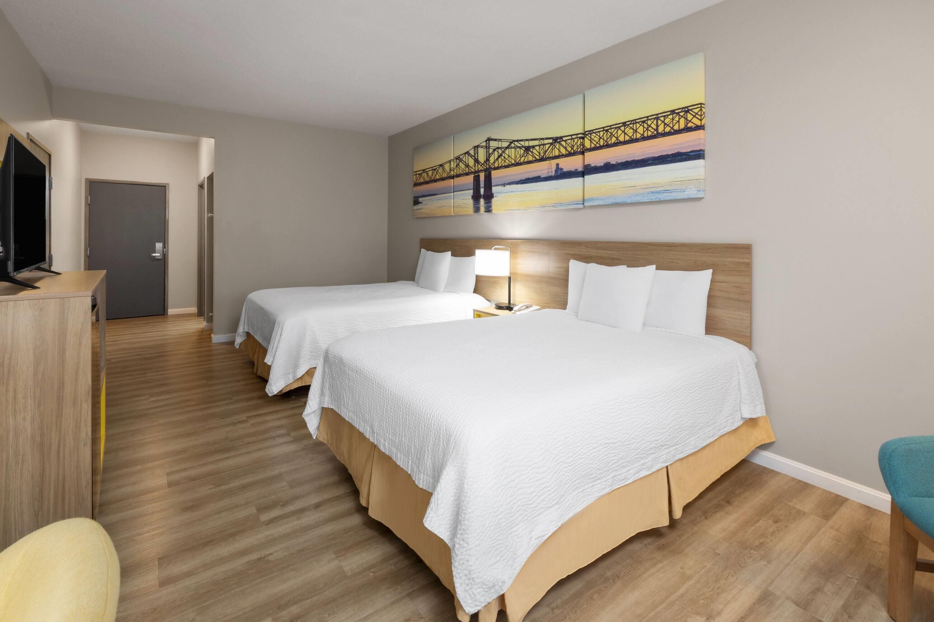 A hotel room with two beds, a TV, a desk, and a painting of a bridge.