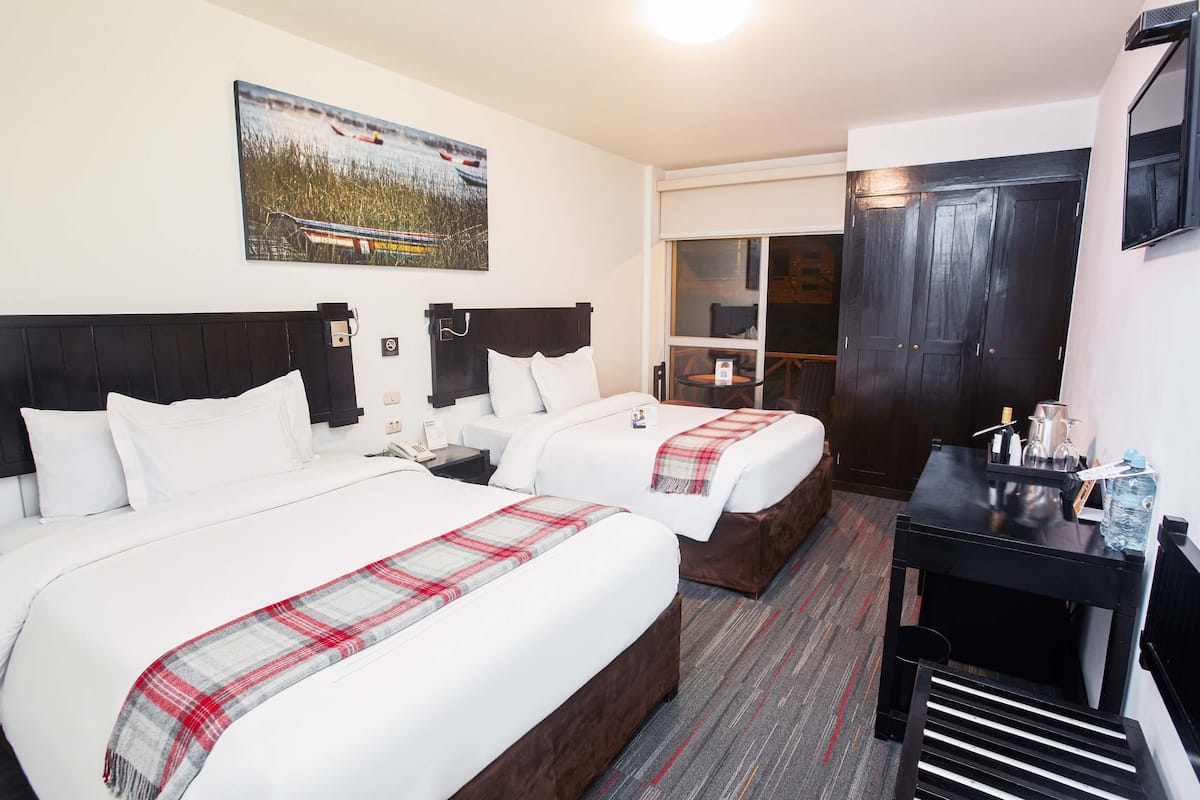 A hotel room with two beds, a desk, a chair, a painting, and a sliding door.