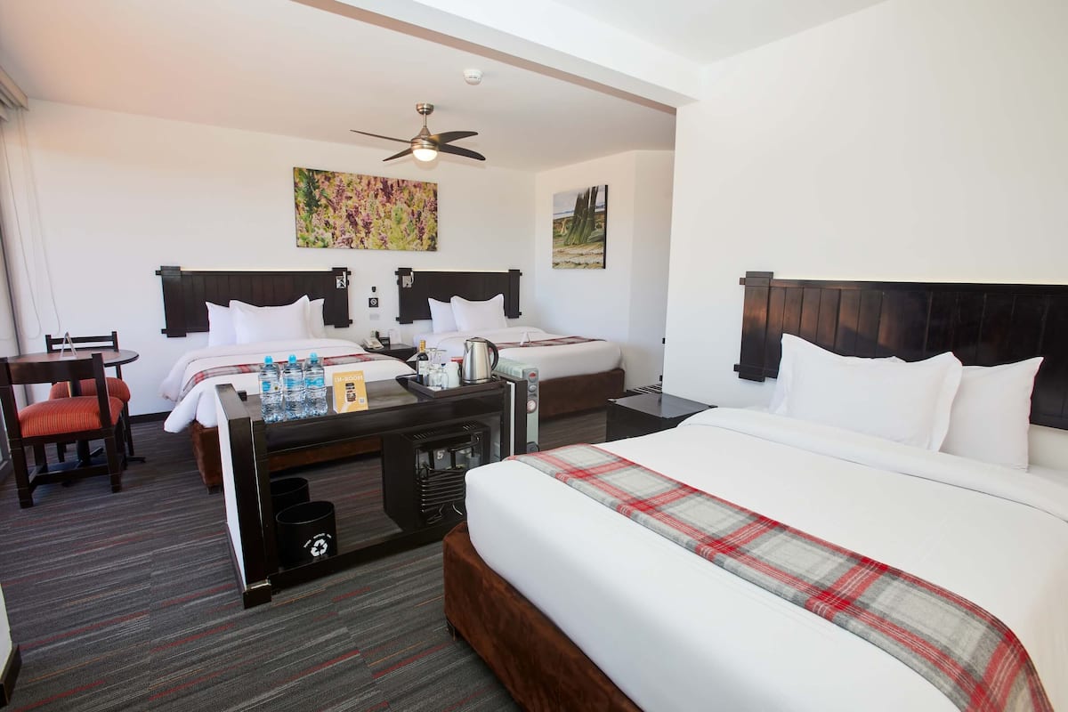 A hotel room with two beds, a desk with a chair, a ceiling fan, and artwork on the walls.