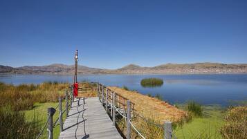 A wooden boardwalk leading to a lake with a clear view of distant hills and a small island.