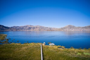 A lake with a boat docked on the shore, surrounded by hills. - Casa Andina Premium Puno (Puno)