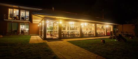 A well-lit building with a covered outdoor dining area and a visible balcony.