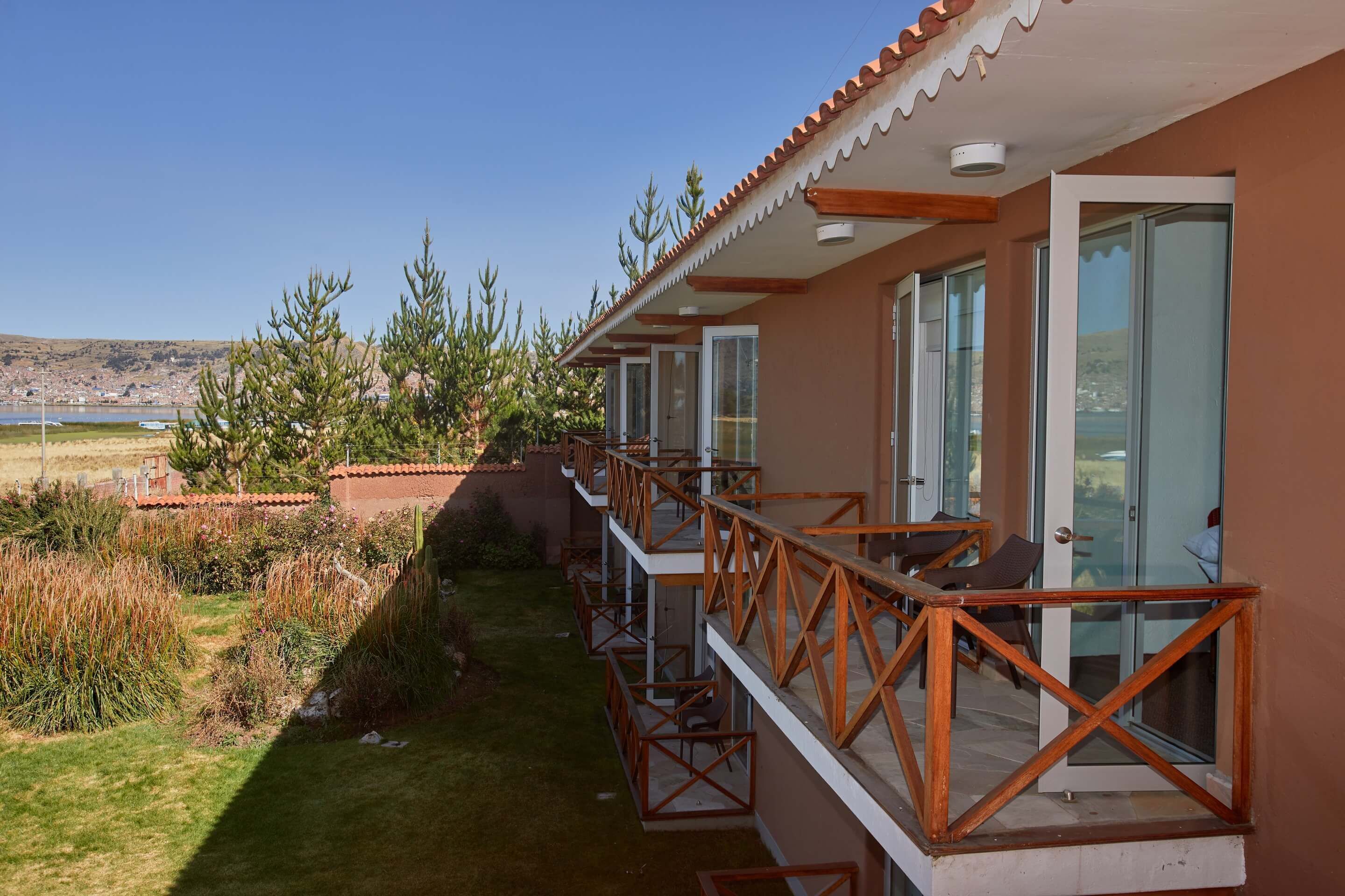 A hotel with a long balcony, clear glass doors, and a view of a lake and hills.