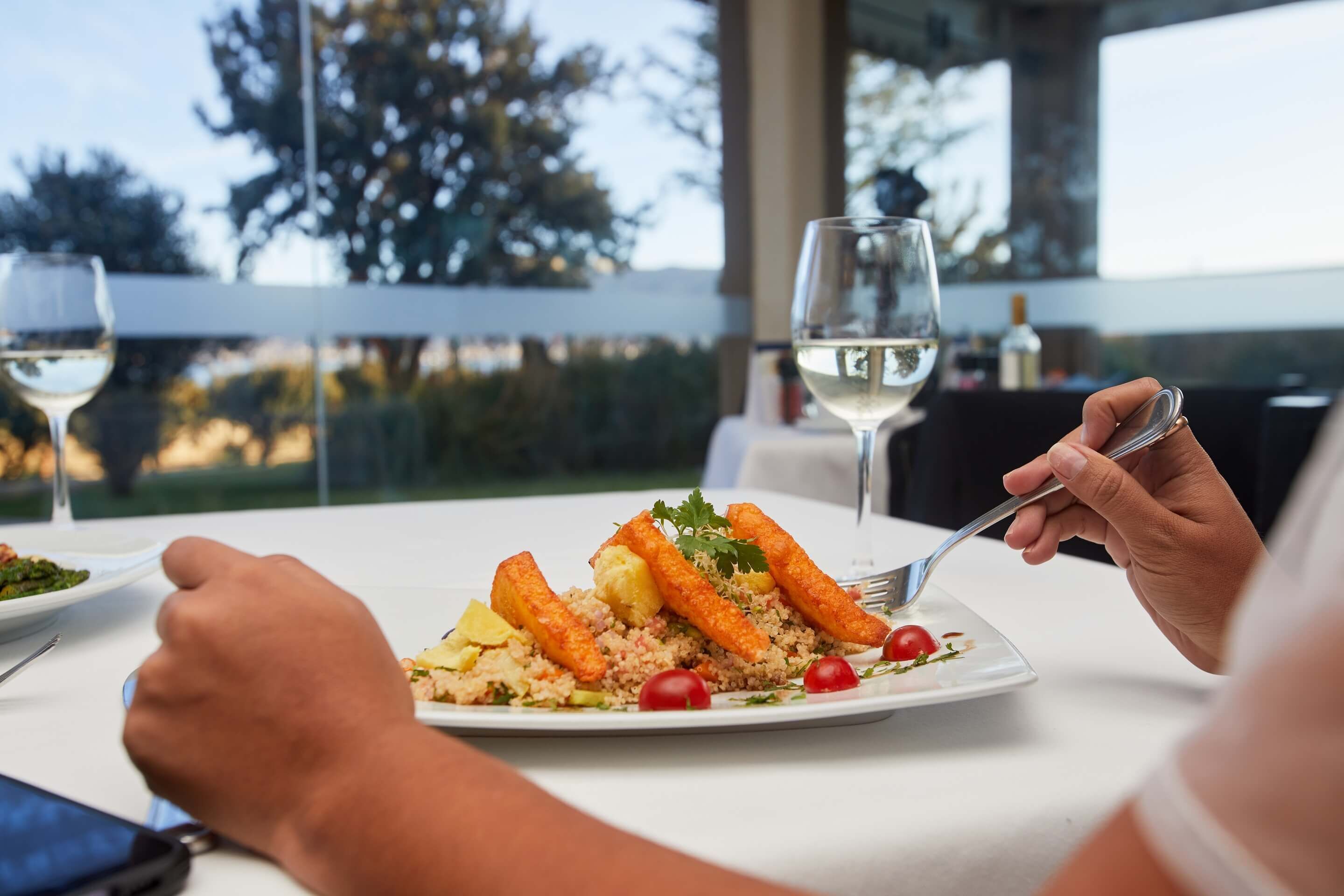 Una mesa de comedor con un plato de comida, una copa de vino blanco y una botella de vino.