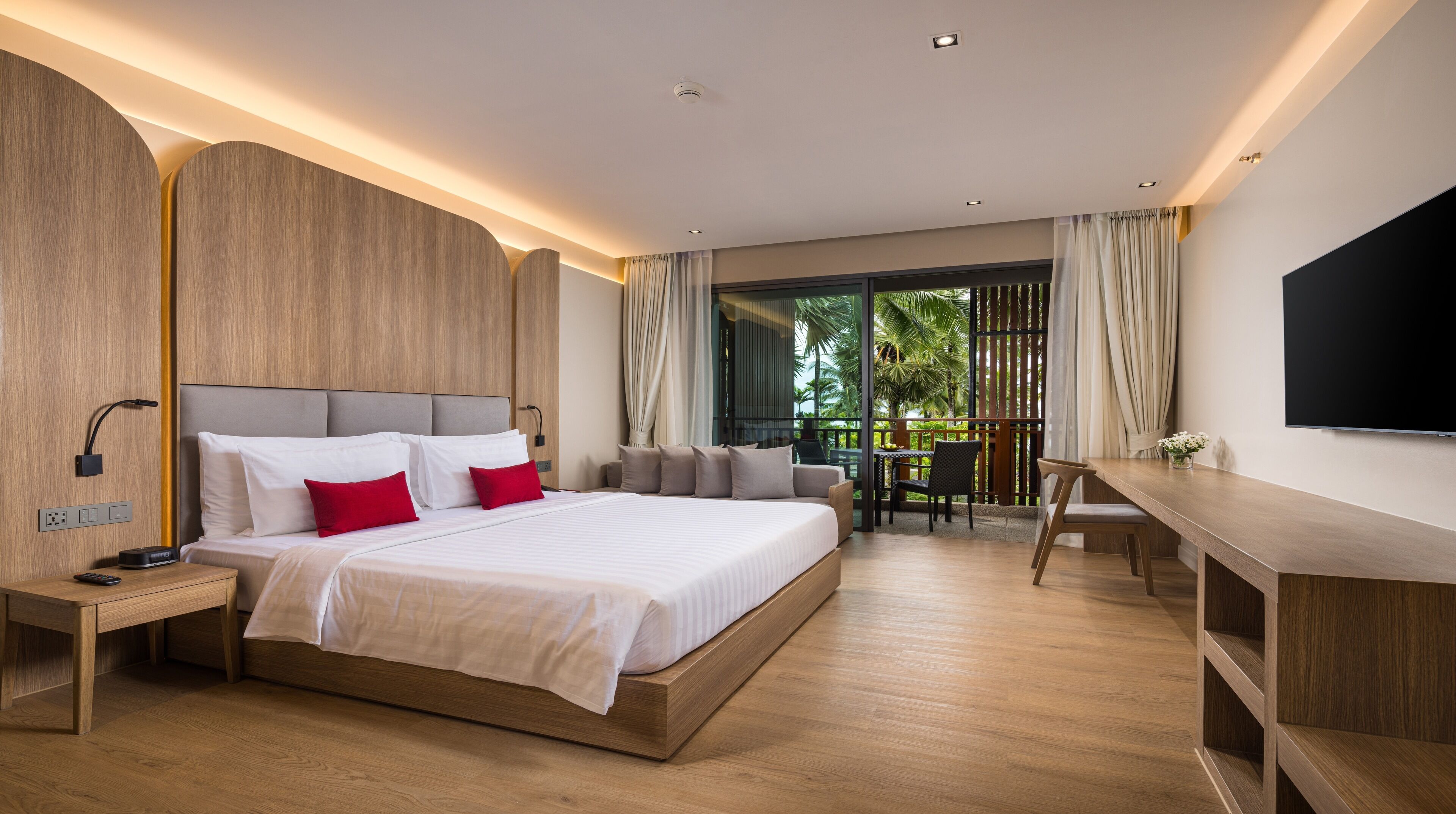 Une chambre d’hôtel moderne dotée d’un grand lit, de tables de chevet, d’un bureau et d’un balcon offrant une vue sur la verdure.