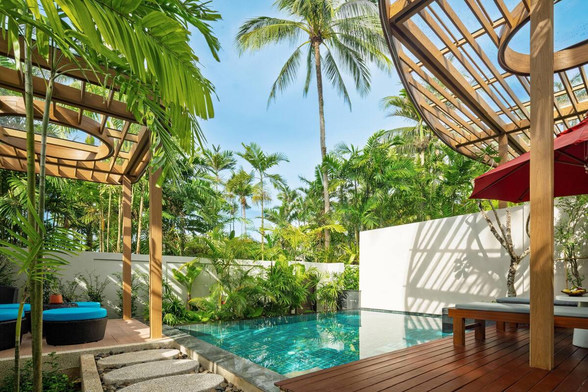 A pool area with wooden deck, lounge chairs, and a pergola structure.