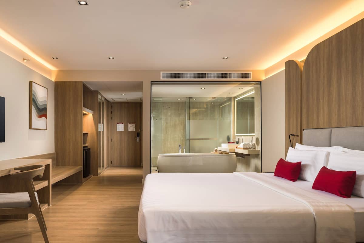 A modern hotel room with a large bed, a desk, a television, and a bathroom with a glass shower.