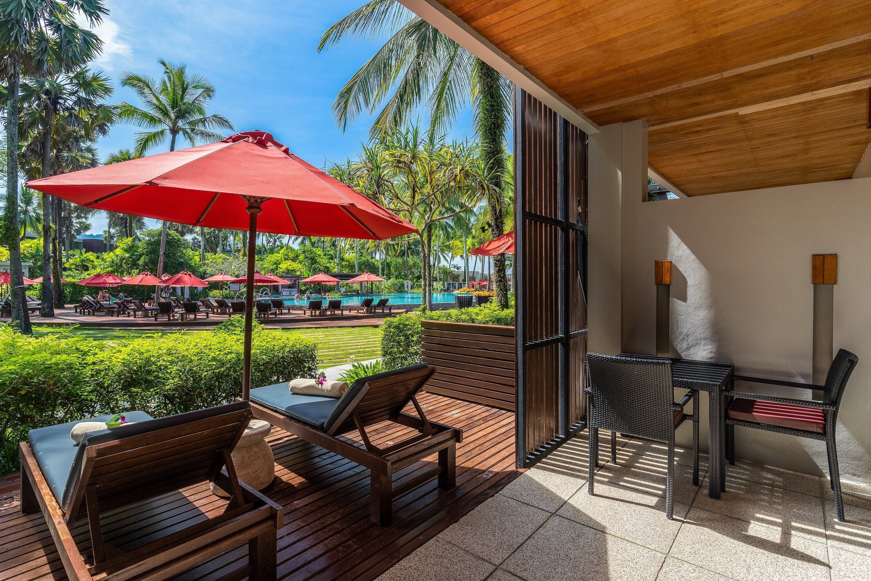 A wooden deck with outdoor seating, a pool, and palm trees.