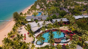 Eine Luftaufnahme von einem Resort mit einem zentralen Schwimmbad, direkt am Strand und üppiger Vegetation.
