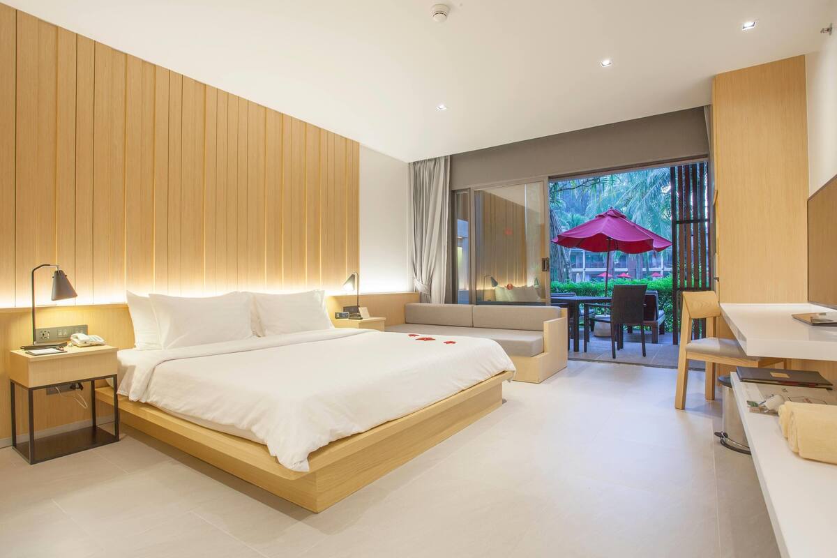 A modern hotel room with a large bed, bedside tables, a desk, and a view of the outdoor area.