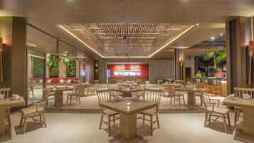 Un restaurante espacioso con varias mesas y sillas, un área de estar central con sofás rojos y un diseño moderno en el techo.