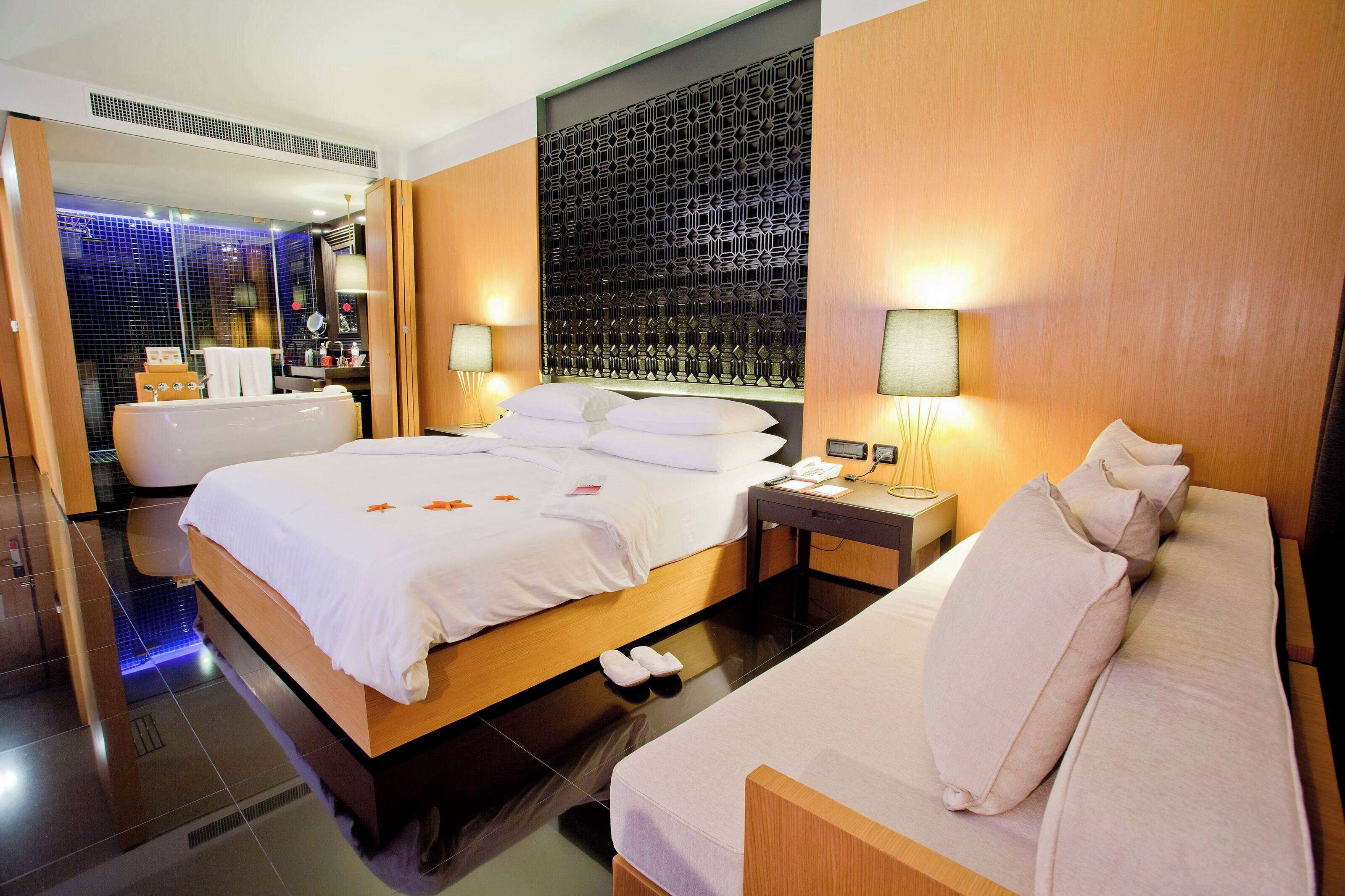 Una habitación de hotel moderna con una cama grande, un sofá, un escritorio y un baño con ducha de vidrio.