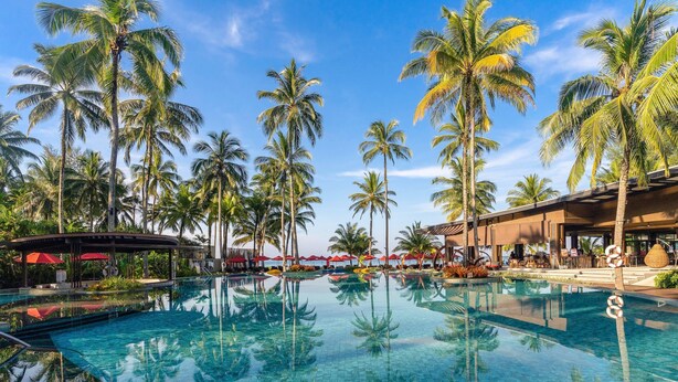 Ein Swimmingpool, umgeben von Palmen und einem Hotelgebäude mit Außenbereich.