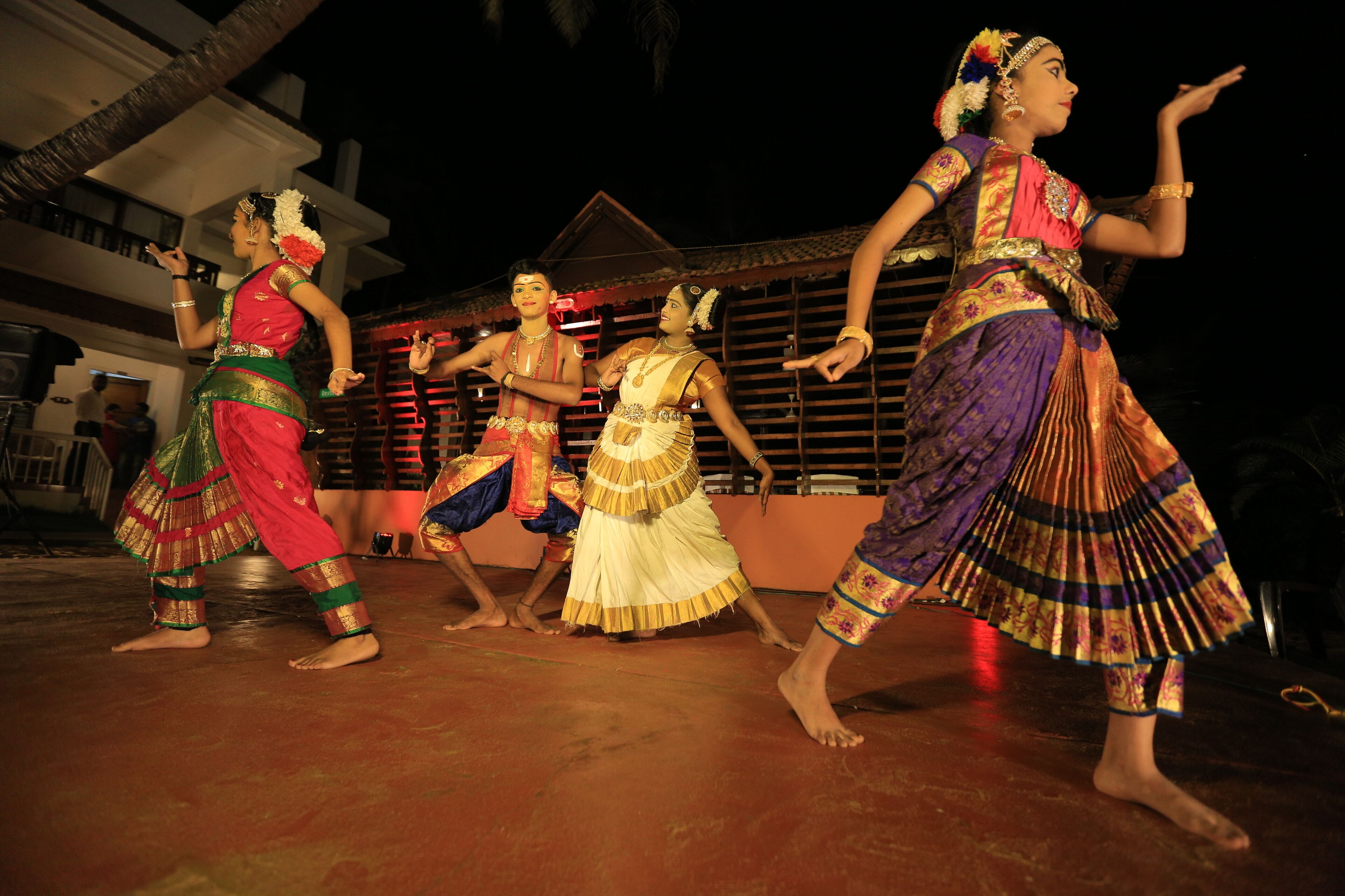 A group of dancers performing on a stage with a traditional building in the background.