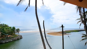 A coastal view with a beach, palm trees, and a rocky shoreline. - Beach and Lake Ayurvedic Resort (Thiruvananthapuram)