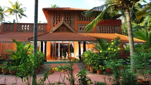 A traditional building with a tiled roof, surrounded by potted plants and palm trees. - Beach and Lake Ayurvedic Resort (Thiruvananthapuram)