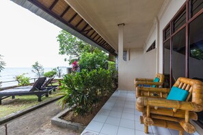 A covered outdoor area with a view of the sea, two lounge chairs, and a bamboo sofa with cushions. - New Adirama Beach Hotel (Banjar)