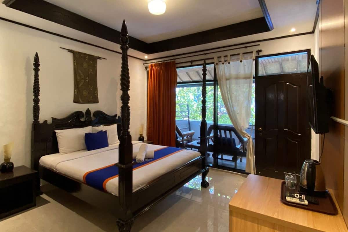 A four-poster bed with a wooden frame, a bedside table with a lamp, and a view of the outdoors through a glass door.