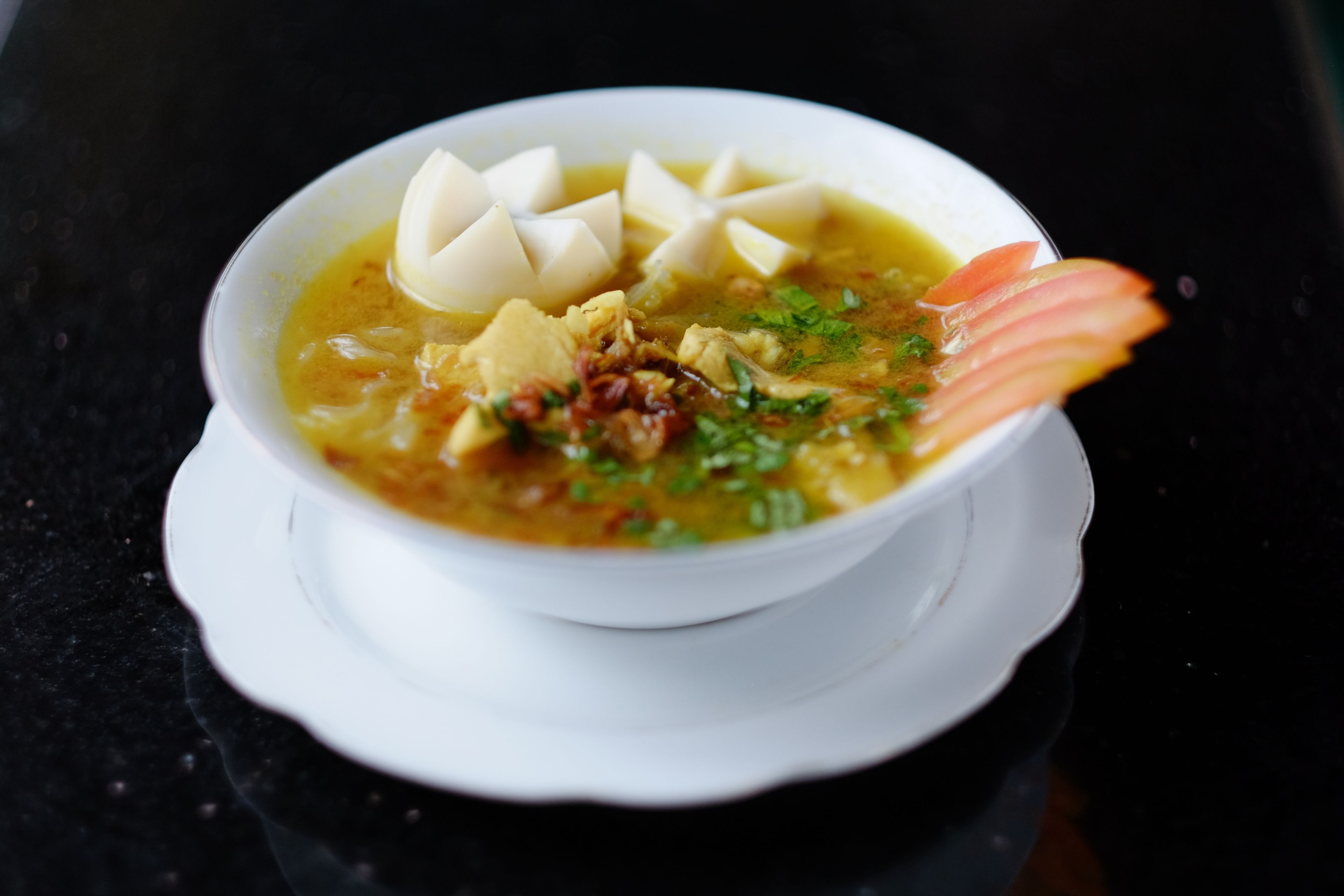 A bowl of soup with tofu and a decorative fish on a white plate.