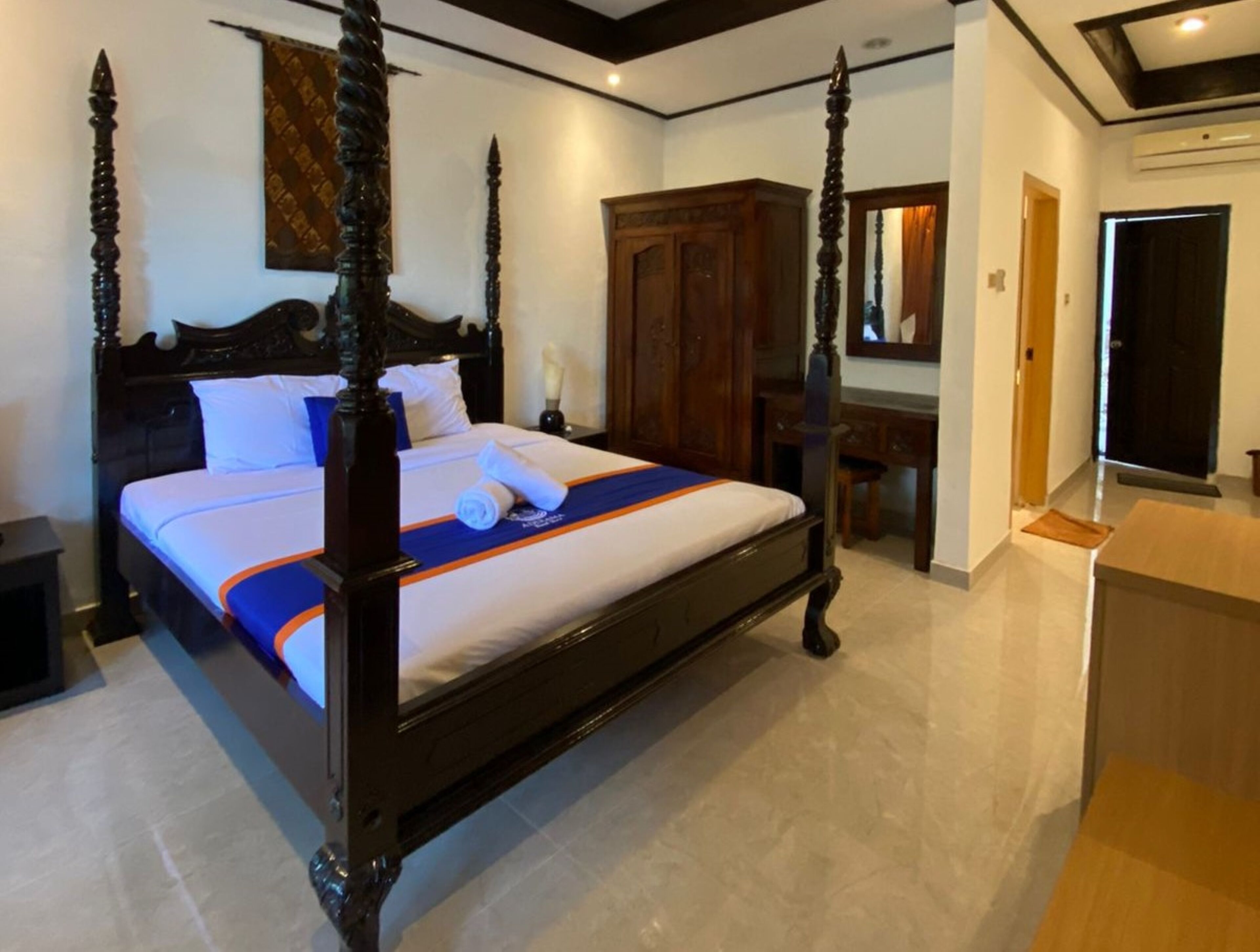 A four-poster bed with a white and blue bedspread, a wooden nightstand, and a wooden wardrobe.