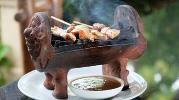 A traditional clay grill with skewers of meat and a bowl of sauce on a plate.