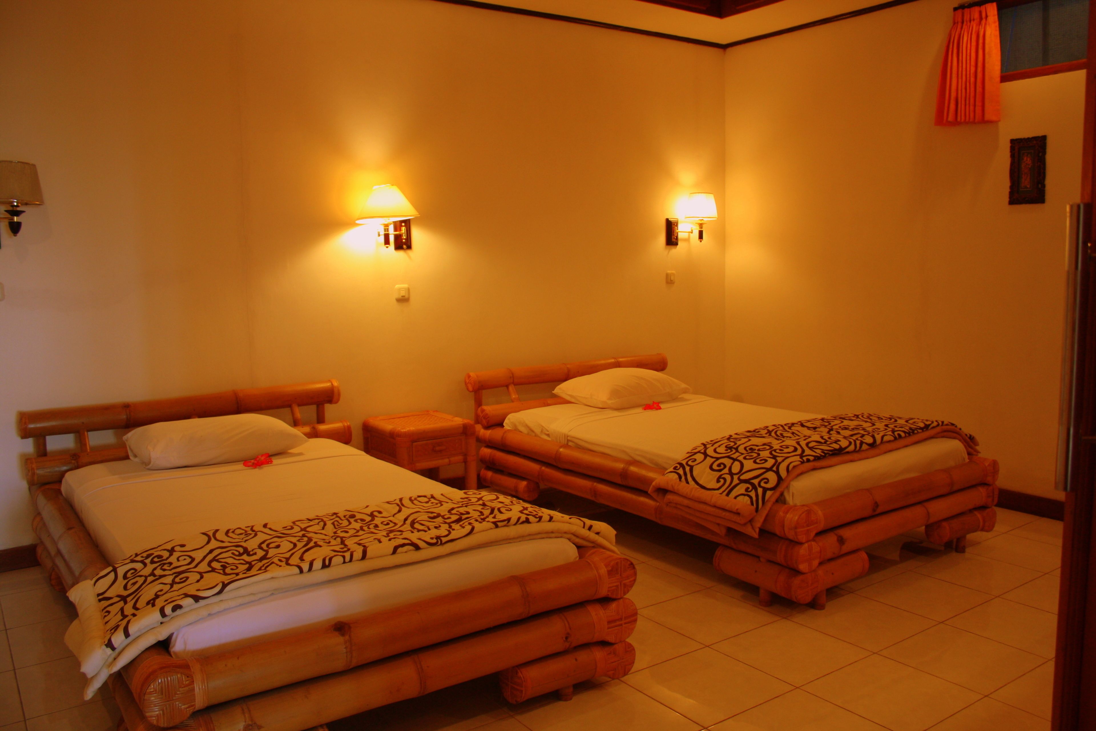 A hotel room with two wooden beds, each with a headboard, bedside tables, and wall-mounted lamps.