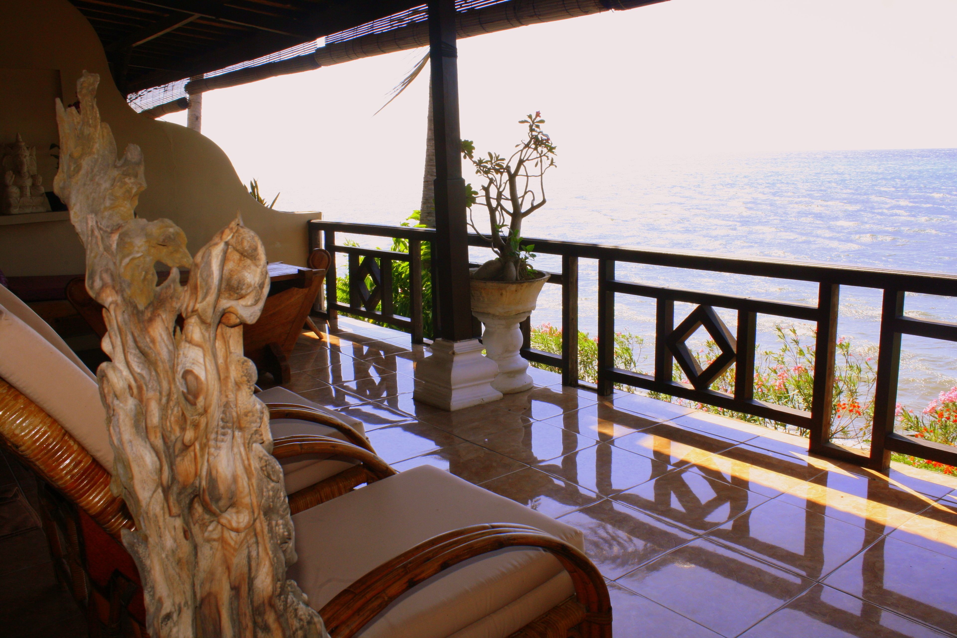 A balcony with wicker chairs and a potted plant, overlooking a body of water.