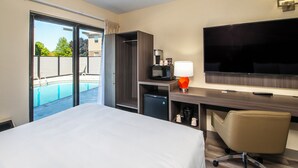 Une chambre d’hôtel équipée d’un lit, d’un bureau, d’une télévision, d’un four à micro-ondes, d’un mini-réfrigérateur et offrant une vue sur une piscine extérieure.