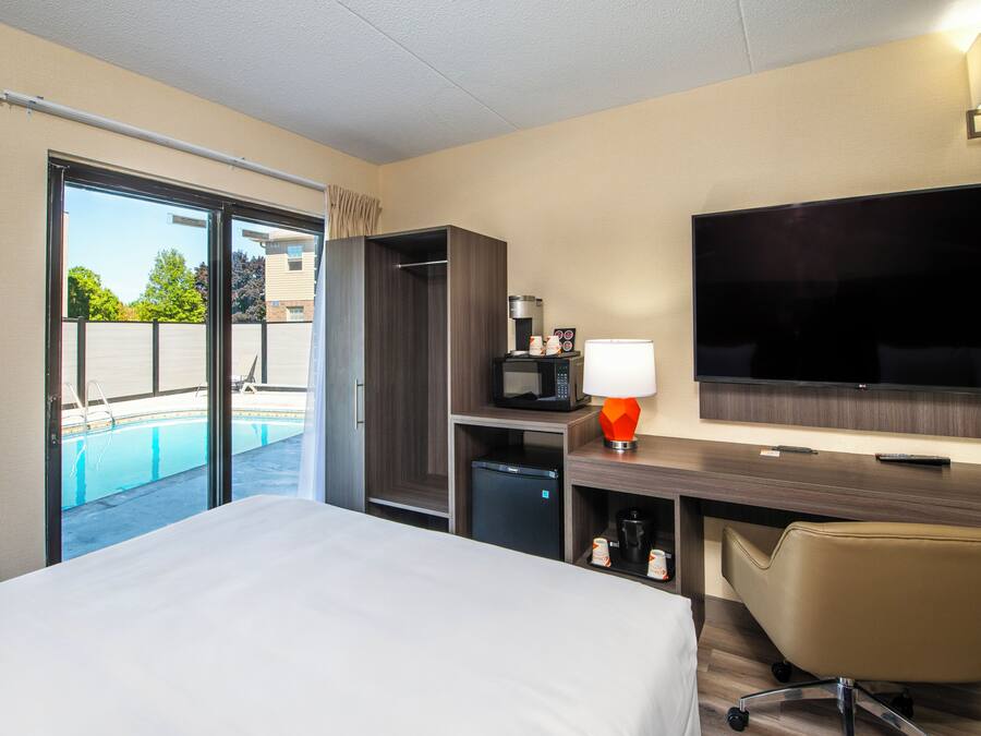 A hotel room with a bed, desk, TV, microwave, mini-fridge, and a view of an outdoor swimming pool.