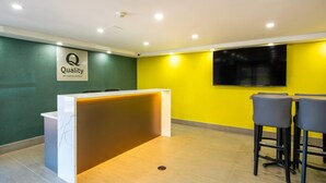 Un espace d’accueil avec un comptoir en marbre, une enseigne indiquant « Qualité garantie par Choice Hotels », un mur jaune et un téléviseur fixé au mur.