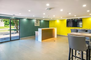 Un hall d’hôtel moderne avec un comptoir d’accueil, un espace salon et un grand écran mural.