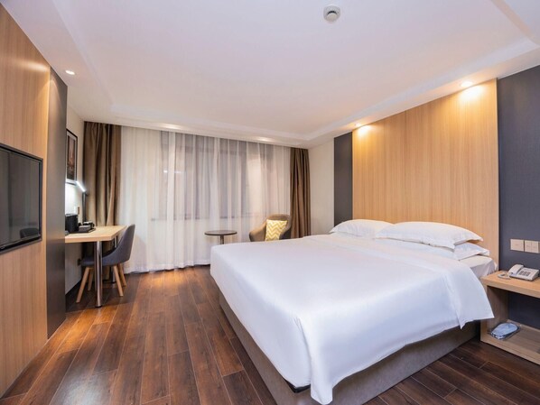 Moderni hotellihuone, jossa on suuri sänky, työpöytä tuolilla, pieni pöytä ja televisio.