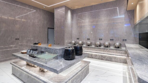 Un espace spa moderne doté d’un sol en marbre, d’un espace de détente central avec une table de massage et de plusieurs salles de vapeur équipées de sièges.
