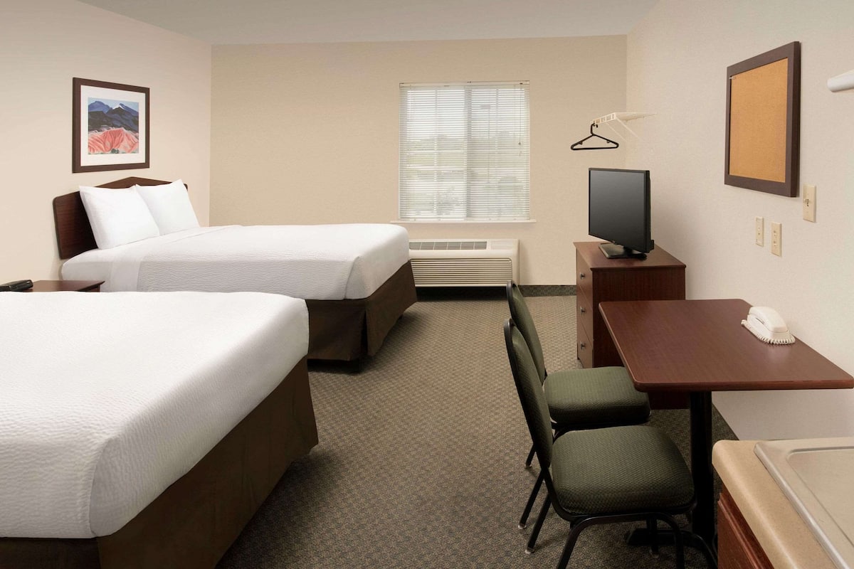 A hotel room with two beds, a desk with a chair, a television, and a window with blinds.