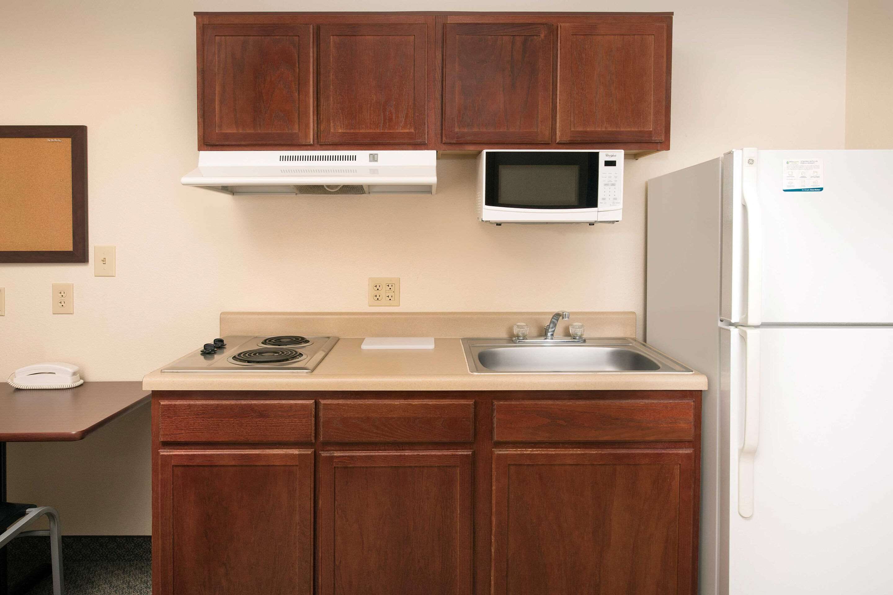 A compact kitchen with wooden cabinets, a microwave, a refrigerator, a sink, and a stove.