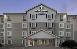 A multi-story hotel with a flat facade, a central entrance, and a parking area in front.