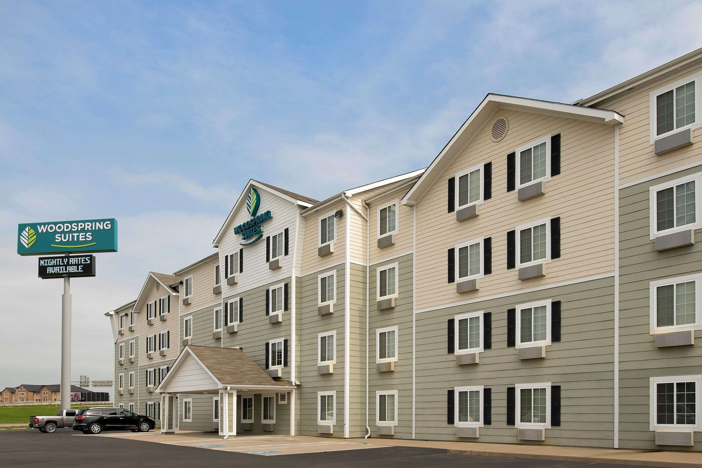 A multi-story hotel with a sign indicating 'Woodspring Suites' and 'Nightly Rates Available'.