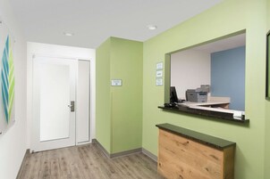 A reception area with a green wall, a wooden counter, a computer, and a printer.