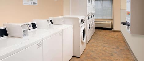 A laundry facility with multiple washing machines and dryers, a service information poster, and a tiled floor.