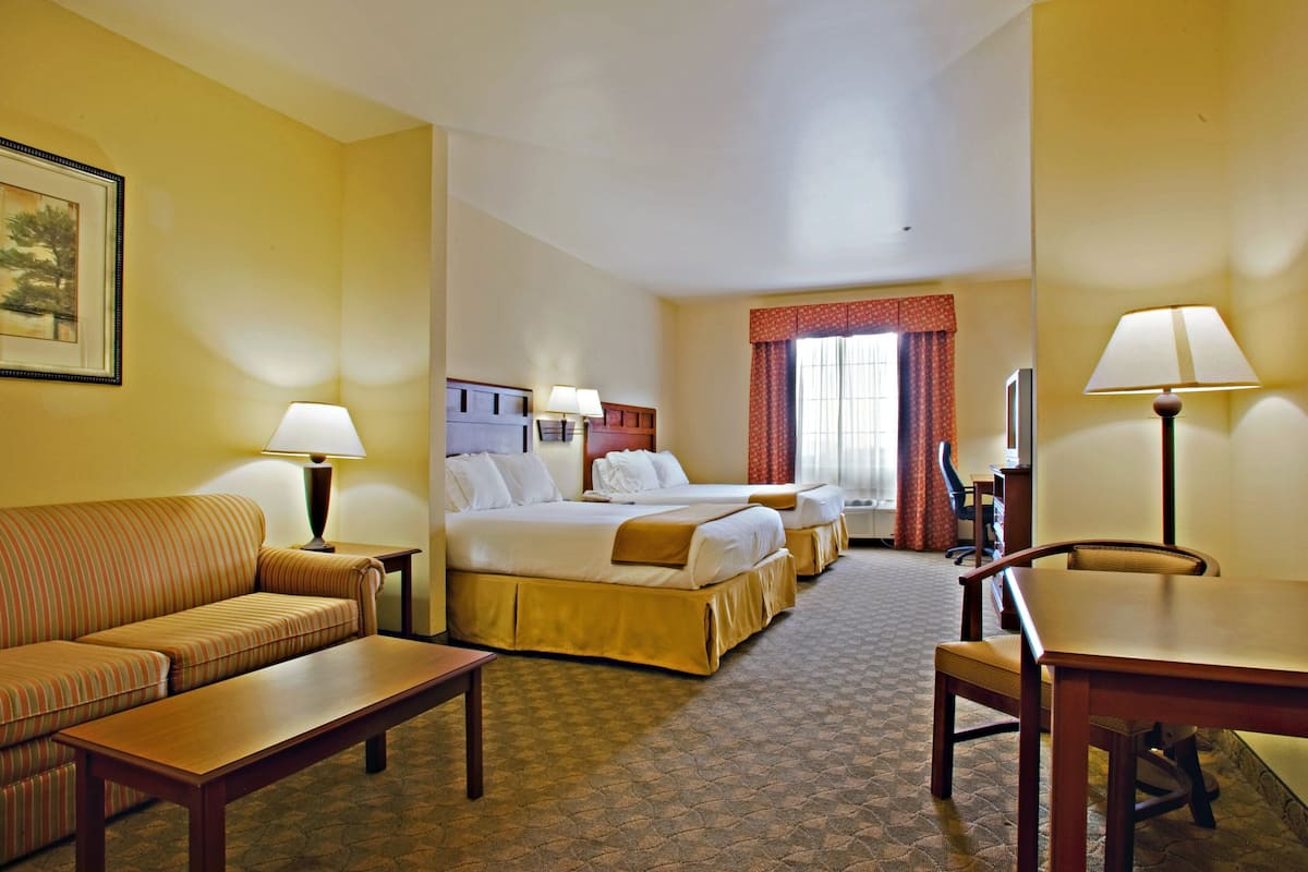 A hotel room with a sofa, two beds, a desk, and a chair.